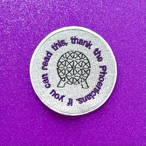 May include: Embroidered patch with a silver border and a purple background. The patch features a geometric sphere design and the text "If you can read this, thank the Phoenicians."