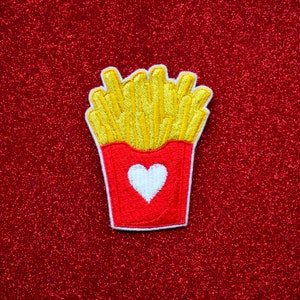 May include: A red and yellow embroidered patch of a container of french fries with a white heart on the front.