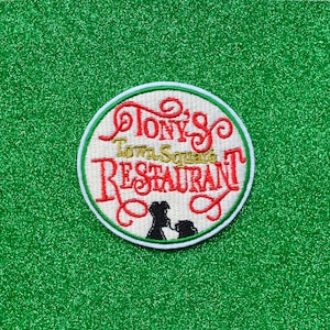 May include: A white and red embroidered patch with the text "Tony's Town Square Restaurant" in a circle. The patch features a black silhouette of a woman and a dog.