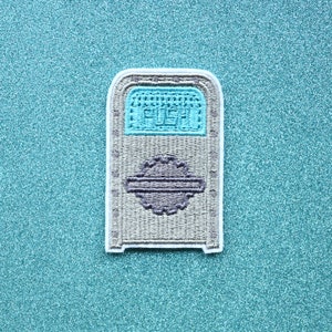 May include: A gray and white embroidered patch of a trash can with the word "PUSH" in blue on the front.