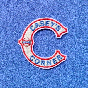 May include: White and red embroidered patch with the text "Casey's Corner" in a blue and white font. A baseball is depicted in the center of the "C".