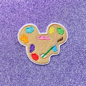 May include: A brown and white embroidered patch of a paint palette with a paintbrush. The palette has colorful paint swatches in shades of red, orange, yellow, green, blue, purple, and pink.