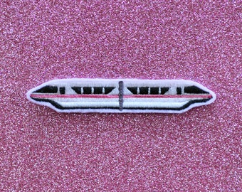 May include: A white and red embroidered patch of a monorail train on a pink glitter background.