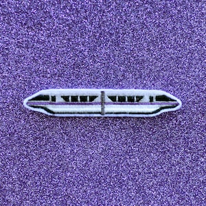 May include: White and purple embroidered patch of a monorail train on a purple glitter background.