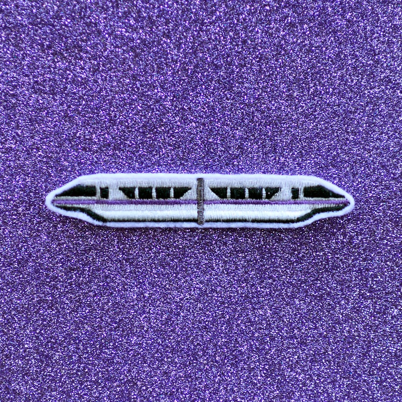 May include: White and purple embroidered patch of a monorail train on a purple glitter background.