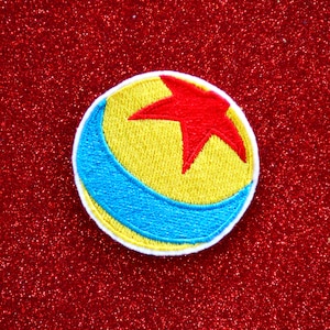 May include: A yellow and blue embroidered patch with a red star in the center. The patch is shaped like a ball with a crescent moon design.