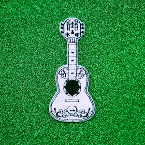 May include: White embroidered guitar with a skull design on a green glitter background.