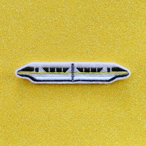 May include: A white and yellow embroidered patch of a monorail train on a yellow glitter background.