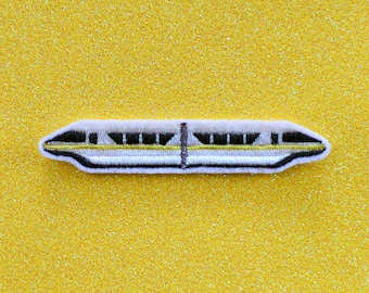 May include: A white and yellow embroidered patch of a monorail train on a yellow glitter background.