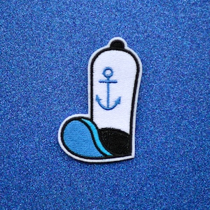May include: A white and blue embroidered patch shaped like a boot with an anchor design. The boot has a blue toe and a black heel.