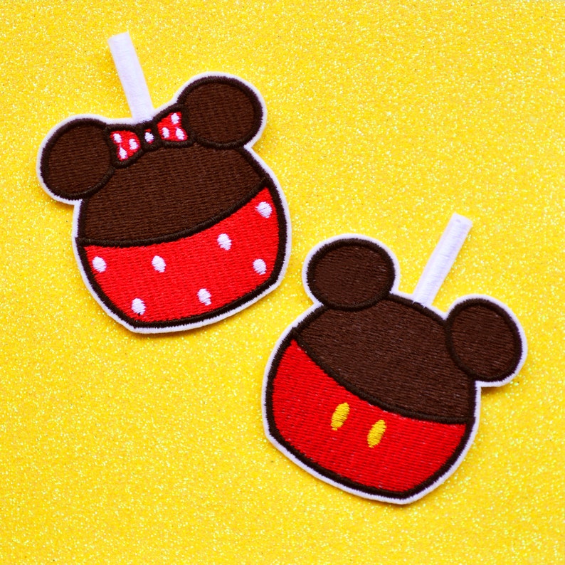 May include: Two embroidered iron-on patches featuring a red and white Mickey Mouse head and a Minnie Mouse head with a red bow. The patches are on a yellow glitter background.