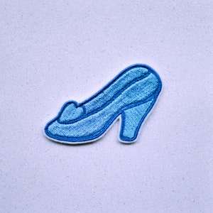May include: A blue embroidered glass slipper with a white outline. The slipper is a popular symbol of Cinderella.