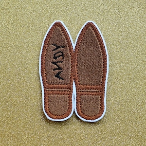May include: A pair of brown embroidered felt slippers with the word "Yay" stitched on one slipper.