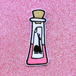 May include: A pink and white embroidered patch of a glass bottle with a cork stopper. The bottle contains a pink liquid and a black silhouette of a llama inside.