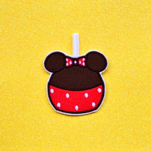 May include: A brown and red felt applique of a cartoon character with mouse ears, a red bow, and white polka dots.