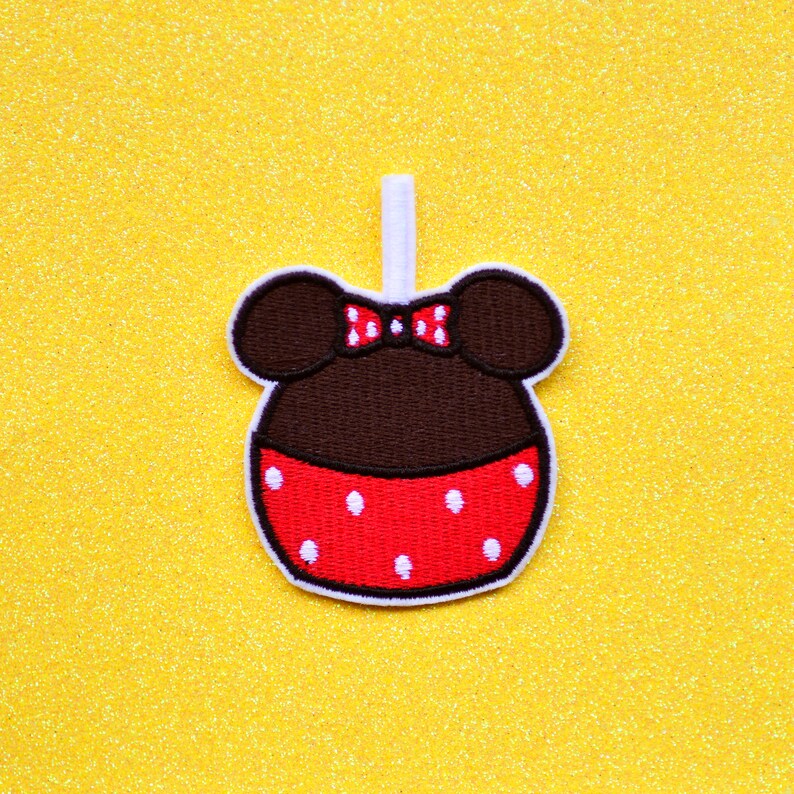 May include: A brown and red felt applique of a cartoon character with mouse ears, a red bow, and white polka dots.