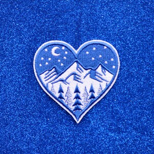 May include: White embroidered mountain scene with a crescent moon and stars on a blue heart-shaped patch.