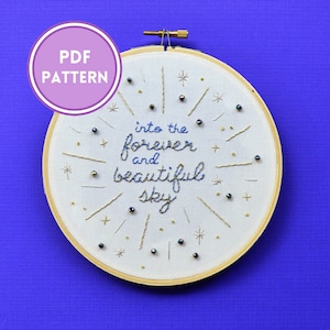 May include: Embroidered hoop art with the text "into the forever and beautiful sky" in blue thread. The hoop is decorated with gold thread and iridescent beads.