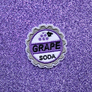 May include: Purple and white embroidered patch shaped like a bottle cap with the words "GRAPE SODA" on it.