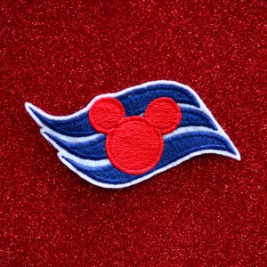 May include: A blue and white embroidered patch with a red Mickey Mouse head in the center. The patch is shaped like a wave and has a white outline.