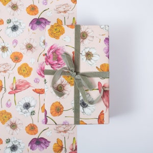May include: A wrapped gift box and wrapping paper featuring a floral pattern with pink, orange, purple, and white flowers. The gift is tied with a sage green velvet ribbon. The background is white.
