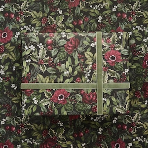 May include: A rectangular gift box wrapped in dark paper featuring a botanical pattern of red flowers, green holly leaves, and white berries. A wide, sage green velvet ribbon is wrapped around the box in a cross pattern.