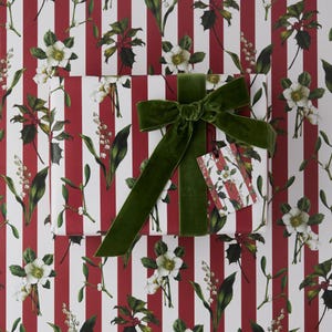 May include: A wrapped gift with a green velvet bow and a matching gift tag. The wrapping paper features a pattern of white flowers and green leaves on a red and white striped background. The gift tag has the same floral pattern.