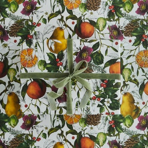May include: Gift-wrapped present on a white background with a repeating pattern of oranges, pears, and flowers. The gift is wrapped in patterned paper and tied with a green velvet ribbon. The paper features illustrations of fruit, flowers, and greenery.