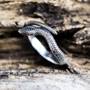 Peut inclure: Une bague en argent en forme de serpent avec un œil en pierre rouge. Le serpent est enroulé autour de la bande de la bague.