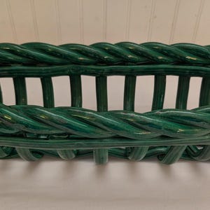 May include: A green ceramic basket with a woven rope design around the rim. The basket has vertical bars forming the sides and a rectangular shape. The basket is approximately 30 cm long, 15 cm wide, and 10 cm tall.