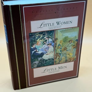 May include: A hardcover book titled "Little Women" and "Little Men" by Louisa May Alcott. The book has a burgundy cover with gold accents and illustrations. The cover features a classic library design.