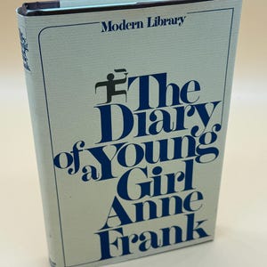 May include: A hardcover book titled "The Diary of a Young Girl Anne Frank" in blue text on a light blue background. The book is from the "Modern Library" series. The cover features a stylized figure.
