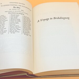 May include: Open book with text from "Gulliver's Travels" by Jonathan Swift. The left page features an ode, and the right page displays "A Voyage to Brobdingnag." The book has a tan cover and pages with text.