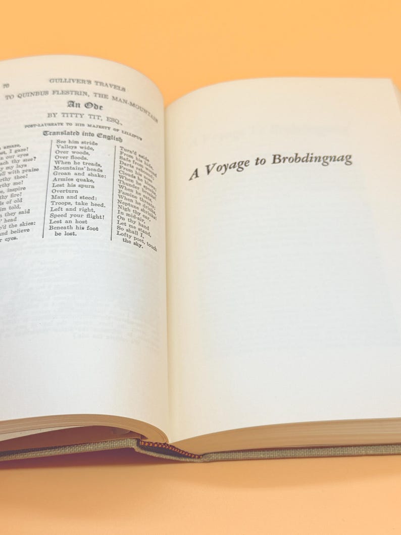 May include: Open book with text from "Gulliver's Travels" by Jonathan Swift. The left page features an ode, and the right page displays "A Voyage to Brobdingnag." The book has a tan cover and pages with text.