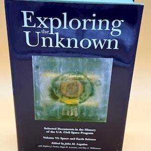 May include: A hardcover book titled "Exploring the Unknown" with a dark blue cover. The book features an image of a circular object with yellow and green hues. The text on the cover includes "Selected Documents in the History of the U.S. Civil Space Program."