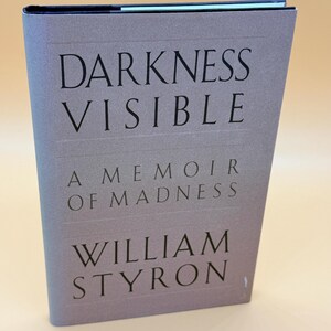 May include: A white ceramic mug with a black handle and the text "But First, Coffee" in a black, handwritten-style font. The mug is on a white surface.