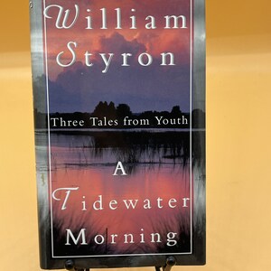 May include: A book titled "A Tidewater Morning" by William Styron. The book cover features a sunset over a body of water with trees in the foreground. The book is part of a series called "Three Tales from Youth".