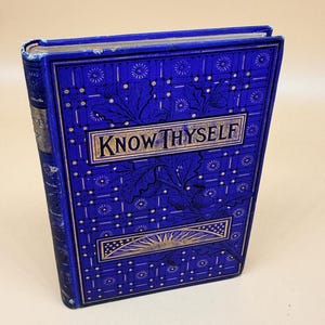 May include: A hardbound book with a vibrant blue cover featuring gold-colored embossed details. The front cover displays the text "KNOW THYSELF" in a rectangular frame, surrounded by intricate patterns of oak leaves, acorns, and small star motifs.