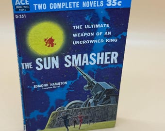 May include: Vintage paperback book titled "The Sun Smasher" by Edmond Hamilton. The cover features a yellow sun with a red design, a futuristic weapon, and running figures against a dark blue starry background. The book is part of the Ace Double Novel series.