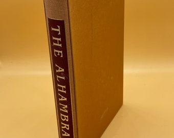May include: A brown book with a spine that reads "THE ALHAMBRA" in gold lettering on a maroon background.