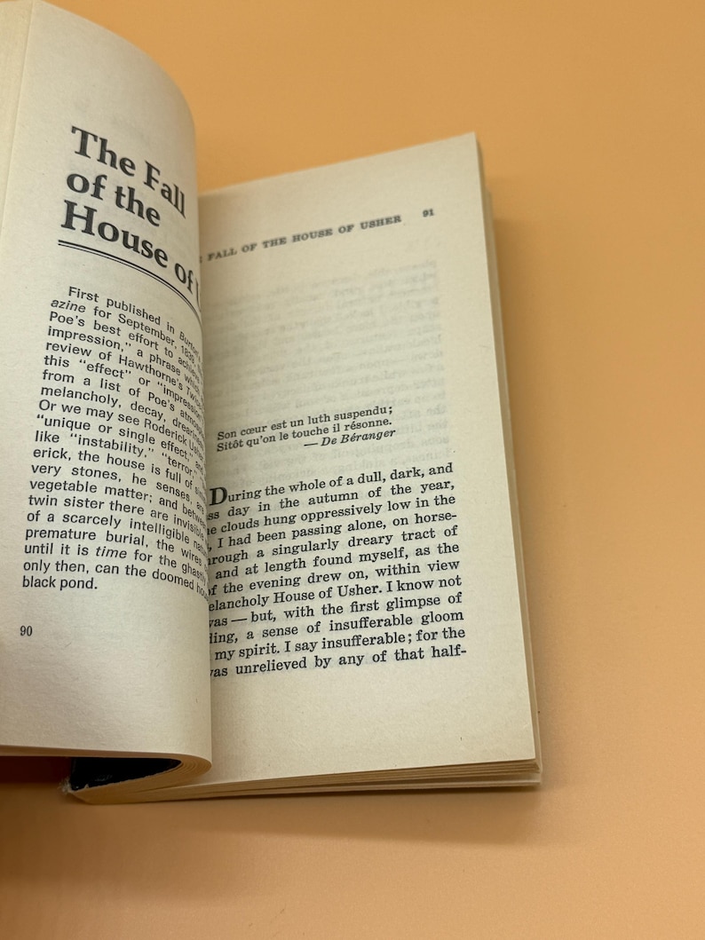 May include: An open book displaying the title "The Fall of the House of Usher" in black text. The pages are off-white, with further text and a French quote. The background is a light orange.