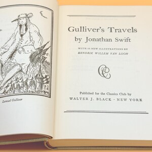 May include: An open book with the title "Gulliver's Travels" by Jonathan Swift. The book has illustrations and text. The publisher is Walter J. Black, New York. The left page shows an illustration of Lemuel Gulliver.