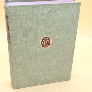May include: A hardcover book with a light green linen cover. The spine is a darker burgundy color. A gold and burgundy emblem is centered on the front cover. The top edge of the book's pages are a light purple color.