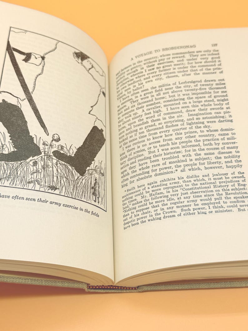 May include: Open book with text and a black and white illustration of figures in a field. The text reads "A Voyage to Brobdingnag" and describes military exercises. The book is open to a double-page spread.