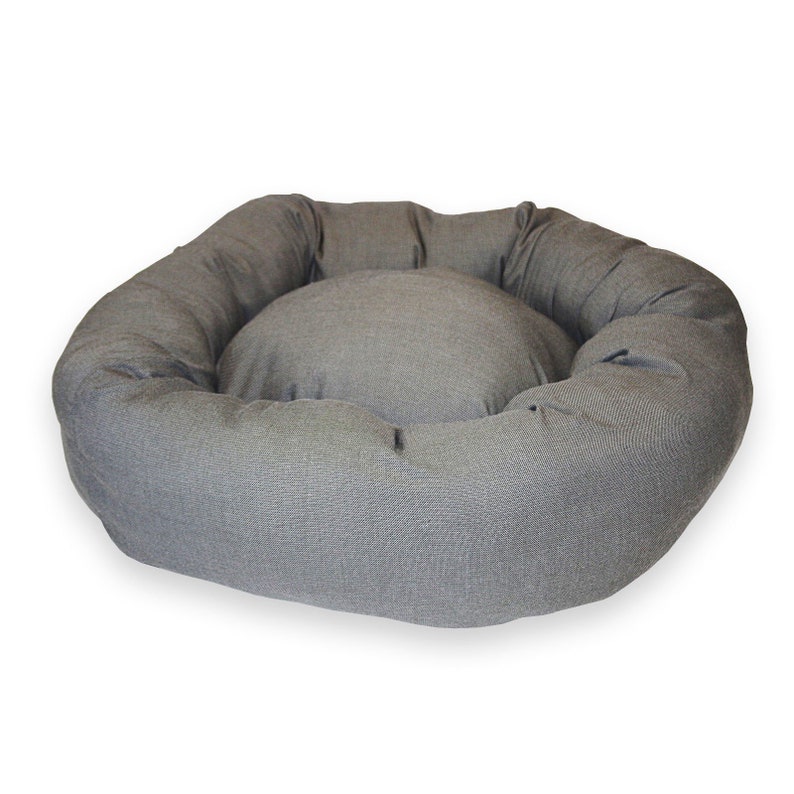 May include: A grey, round pet bed with a raised rim and a soft, plush interior. The bed is made of a durable fabric and is perfect for providing a comfortable and cosy sleeping space for your pet.