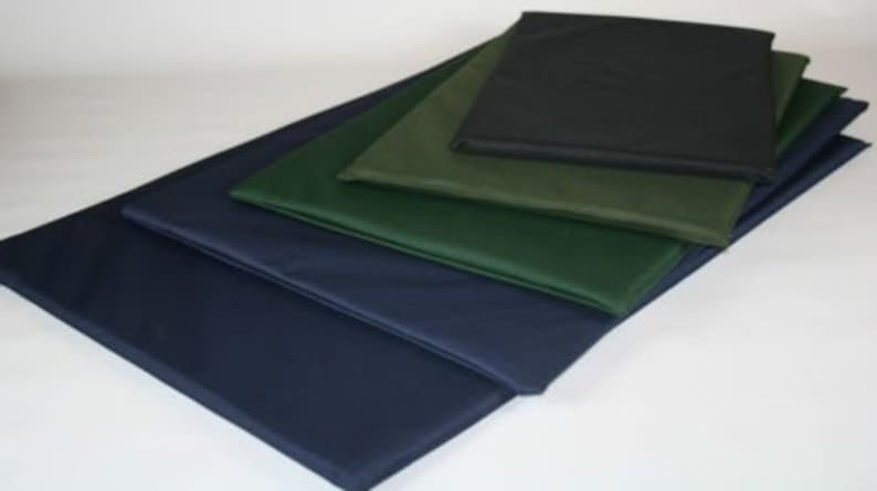 May include: An assortment of rectangular cushions in various sizes and colors. The cushions are stacked, showcasing shades of navy blue, green, and black. The cushions appear to be made of a smooth, possibly waterproof material.