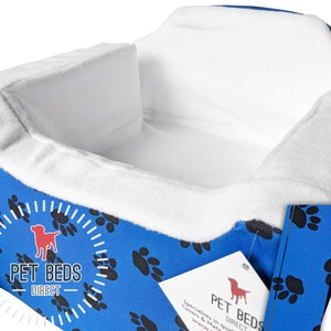 Puede incluir: Cama para perro azul y blanca con diseño de huella de pata. La cama tiene un borde elevado y un forro blanco suave. La cama está etiquetada como "Pet Beds Direct".