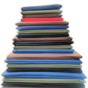 May include: A stack of folded fabric in various colors, including blue, green, brown, red, and black. The fabrics are neatly arranged in a layered pile, showcasing a range of hues and textures. The image is set against a plain white background.