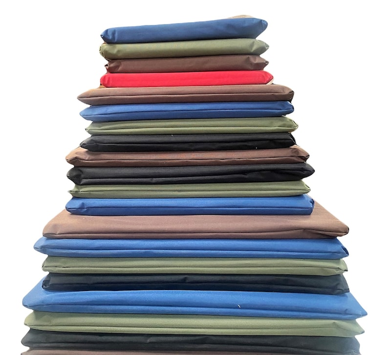 May include: A stack of folded fabric in various colors, including blue, green, brown, red, and black. The fabrics are neatly arranged in a layered pile, showcasing a range of hues and textures. The image is set against a plain white background.