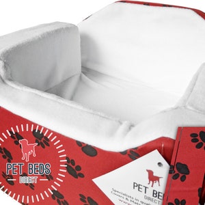 Puede incluir: Cama para perro roja y blanca con diseño de huella de pata. La cama tiene un borde elevado y un forro blanco suave. La cama está hecha por Pet Beds Direct.